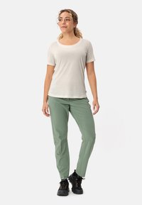 Camicia grigio chiaro a maniche corte con scollo rotondo abbinata a pantaloni flessibili verde oliva e scarpe da trekking nere, che mostrano un look casual per l'outdoor.