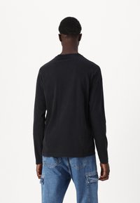 Svart langermet skjorte laget av bomull, med rund hals og avslappet passform. Kombinert med lyseblå cargo-jeans.