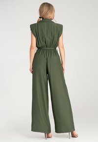 Olive'owy kombinezon z szerokimi nogawkami, krótkimi rękawami i paskiem w talii. Lekka tkanina o gładkiej fakturze i minimalnym wykończeniu.
