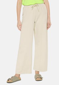 Beige wide-leg pants made of soft fabric, featuring a drawstring waistband. Paired with green slide sandals. No visible patterns.