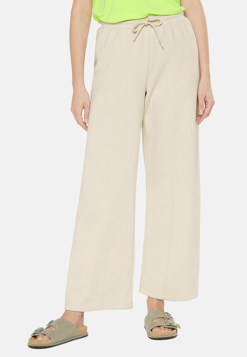 Beige wide-leg pants made of soft fabric, featuring a drawstring waistband. Paired with green slide sandals. No visible patterns.
