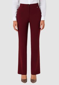 Pantaloni color mogano con taglio su misura, fronte piatto e leggero svasamento sul fondo. Presentano una chiusura con bottone e dettagli discreti sulle tasche.