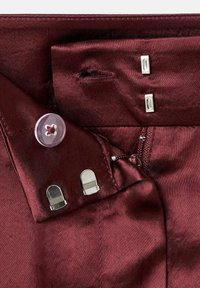 Bordeaux satijnen stof met een doorzichtige knop met een bloemenpatroon, zilverkleurige hardware waaronder twee clips en een rits, en een gladde textuur.