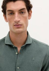 Camisa verde de cuello hecho de tejido texturizado con cierre de botones, presenta un pequeño logotipo bordado en el pecho y un corte relajado.