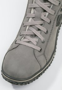 Gray leather shoe with rounded toe, textured surface, and flat gray laces. Features black accents and a patterned rubber sole.