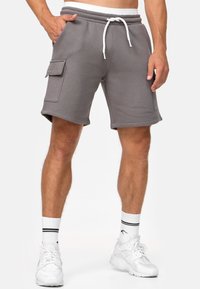 Shorts gris en mélange de coton avec une ceinture élastique, un cordon de serrage ajustable et des poches cargo latérales. Texture lisse et coupe jusqu'aux genoux.