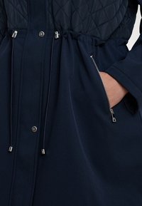 Navy jacket featuring a quilted upper section, drawstring waist, and zippered side pockets with silver hardware accents.