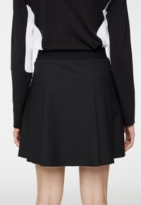 Czarna plisowana spódnica o gładkiej fakturze, z elastycznym pasem i niewidocznym zamkiem z tyłu. Brak widocznych wzorów lub akcentów.