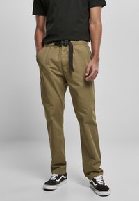 Pantalones de algodón verde oliva con cintura elástica y un cinturón de tela negro, combinados con zapatillas de deporte blancas y negras.