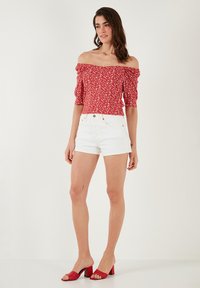 Red floral off-the-shoulder top with puffed sleeves, paired with white denim shorts. Model wears red block-heeled sandals.