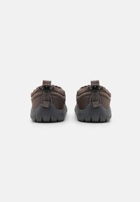 Bruna vadderade slip-on-skor med en texturerad bakre häl som har en dragflik och en flexibel, mönstrad gummisula.