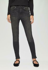 Zwarte skinny jeans met een middelhoge taille, voorzien van vijf zakken en een licht vervaagde afwerking. Gecombineerd met zwarte platte schoenen.