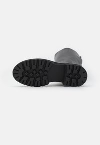 Black rubber boot sole with a textured, tread pattern for grip, featuring deep grooves and ridges for traction and stability.