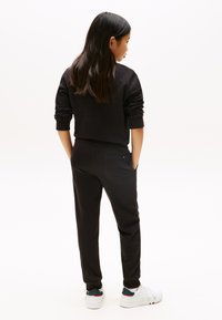 Ensemble de sweat-shirt noir et de joggings, avec une coupe décontractée, des poignets côtelés et des poches latérales, associé à des baskets blanches.