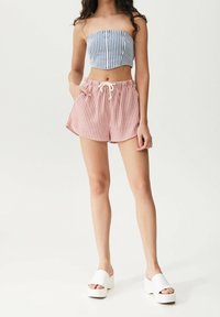 Trägerloses Croptop mit blau-weißen Streifen, kombiniert mit rot-weißen gestreiften Shorts. Weiße Plattform-Slidesandalen vervollständigen den Look.