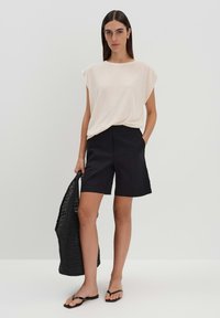 T-shirt a maniche corte color beige chiaro, pantaloni corti neri a vita alta, borsa tote nera intrecciata e infradito neri. Fit semplice e rilassato.