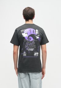 Czarna bawełniana koszulka z krótkim rękawem z kolorowym nadrukiem na plecach, przedstawiającym postacie i tekst w purpurowym i białym kolorze.