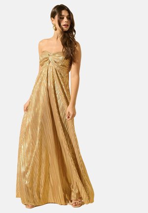 Robe maxi sans bretelles en or avec texture plissée, dotée d'un détail en torsade au niveau du buste et d'un tissu fluide. Accentuée par des boucles d'oreilles.