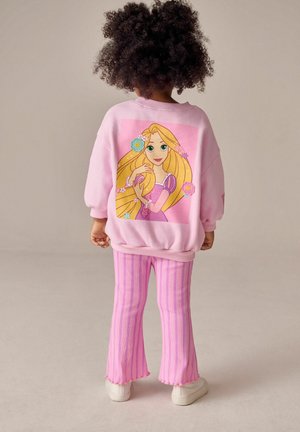 Rosa Sweatshirt mit einem Rapunzel-Graphic auf dem Rücken, kombiniert mit rosa gestreiften Schlaghosen. Die Schuhe des Kindes sind weiße Sneakers.