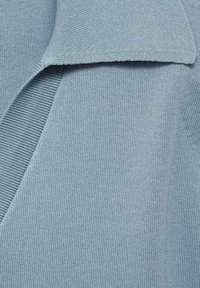 Ljust blått stickat tyg som visar en ribbad textur, med en vikkrage och slät finish. Inga distinkta mönster eller detaljer synliga.