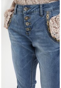 Blå denimjeans med hög midja, fyrknappsstängning och dekorativ söm längs fickorna. Tyget har en mjuk textur.
