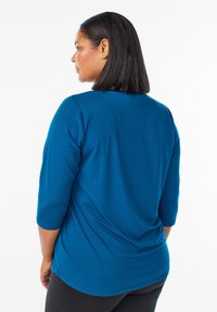 Teal top met driekwartmouwen, gemaakt van soepele stof, met een ronde halslijn en een losse pasvorm die tot de heupen reikt.