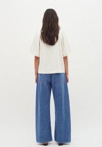 Cream short-sleeve top with a straight hem paired with wide-leg blue denim jeans featuring back pockets and slight fade.