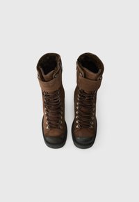 Brązowe skórzane buty trekkingowe z metalowymi oczkami, sznurówkami i gumowym noskiem. Na górze widoczna futrzana podszewka oraz wyściełany kołnierz wokół kostki.