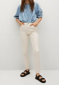 Vaaleanbeiget istutetut housut yhdistettynä siniseen denim-paitaan, jossa on puffihihat ja napillinen etuosa, käytetty mustien sandaalien kanssa.