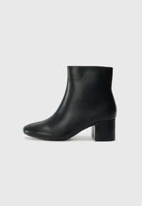 Crne kožne čizme do članaka s uskim vrhom i debelim potplatom. Glatka tekstura s minimalnim detaljima i elegantan, prilagođen dizajn.