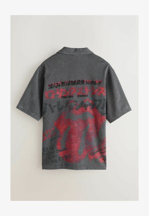 Tricou cu mânecă scurtă, gri cărbune, cu grafică roșie a limbii Rolling Stones. Prezintă texte și modele diverse pe spate. Material în stil vintage.