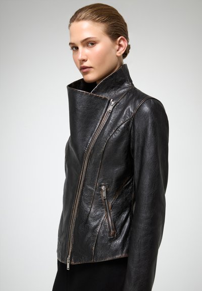 Chaqueta de cuero negro con un alto cuello, cierre de cremallera asimétrico y bolsillo lateral con cremallera. Textura suave con un diseño minimalista.