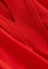 Rode stof met een gladde textuur en subtiele glans. Beschikt over gestikte naden en een lichte drape. Het ontwerp lijkt lichtgewicht en luchtig.