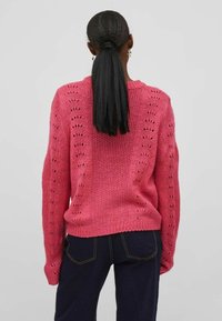 Maglione rosa lavorato a maglia con un motivo testurizzato e dettagli in pizzo, maniche lunghe e orlo a coste. Mostrato da dietro.