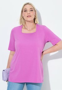 T-shirt rosa a maniche corte con scollatura quadrata, realizzata in tessuto morbido, abbinata a jeans azzurri chiari e a una borsa in lavanda trapuntata.