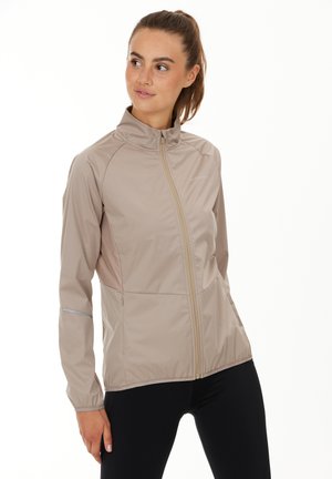 Veste de sport légère, beige, avec un col haut, une fermeture éclair sur toute la longueur à l'avant et des accents réfléchissants sur les manches. Texture lisse, design ajusté.
