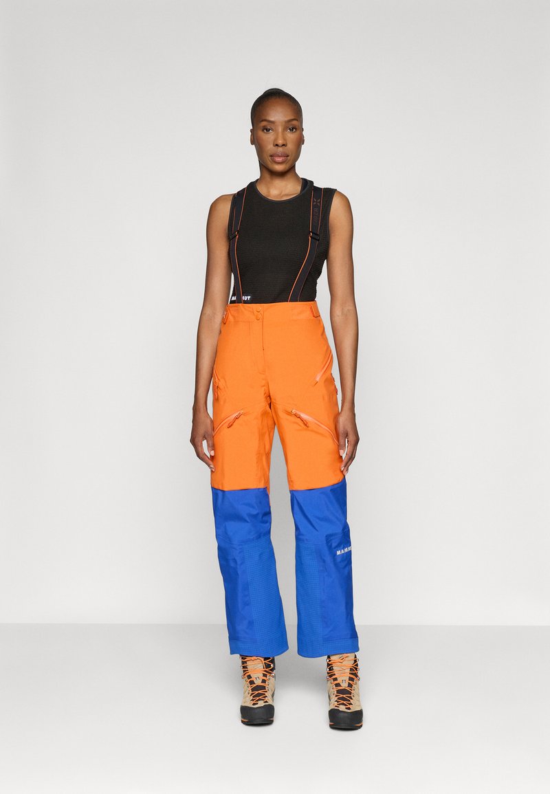Pantaloni da sci arancioni e blu con cerniere e bretelle, tessuto strutturato, dotati di ginocchia rinforzate e orli regolabili.