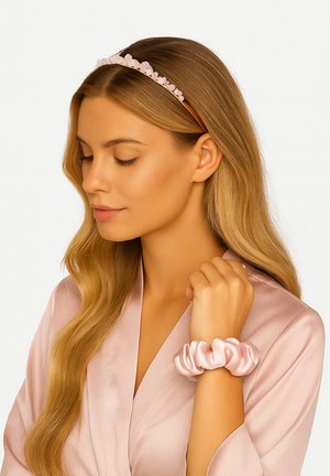 Kobieta o długich blond włosach nosi różową opaskę w kwiaty i pasującą różową satynową gumkę na nadgarstku, ubrana w różowy satynowy szlafrok.