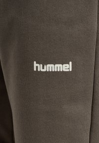 Donkergrijze joggers gemaakt van ribbelstof; heeft een witte "hummel" logo gedrukt aan de linkerkant. Eenvoudig ontwerp zonder verdere patronen.