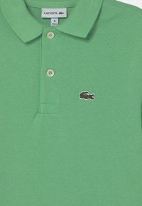 Polo verde realizzato in tessuto texturizzato, con colletto, patta con tre bottoni e logo del coccodrillo ricamato sul petto sinistro.