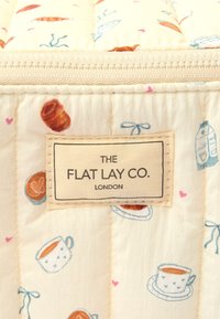 Tkanina pikowana z różnorodnymi ilustracjami jedzenia, w tym filiżankami i ciastkami, w delikatnych pastelowych kolorach z etykietą "THE FLAT LAY CO.".