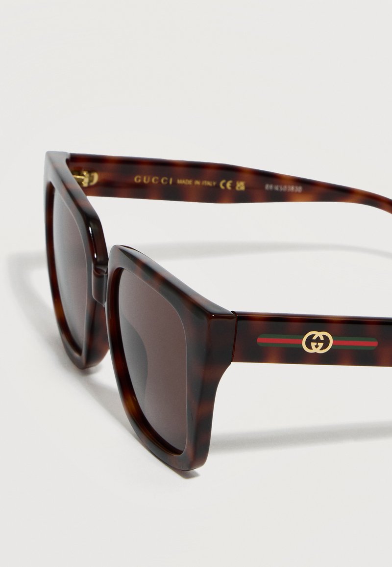 Tortoiseshell square sunglasses with dark lenses, featuring Gucci logo and green-red-green stripes on the temple arms.