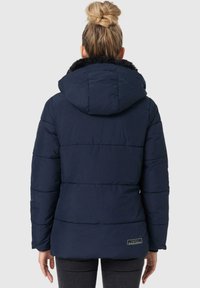 Marineblauwe pufferjack met een capuchon, voorzien van een nepbontkraag, horizontale stiksels en een klein logo-opdruk op de achterkant.