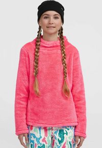 Løst pink fleece-pullover med høj krave og lange ærmer. Stoffet er blødt og har en tekstureret overflade. Stylet med mønstrede bukser.