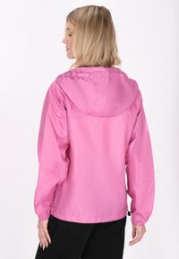 Giacca a cappuccio rosa in materiale leggero e liscio. Presenta polsini elastici e orlo regolabile, con un design semplice e pulito. Senza motivi o accenti.