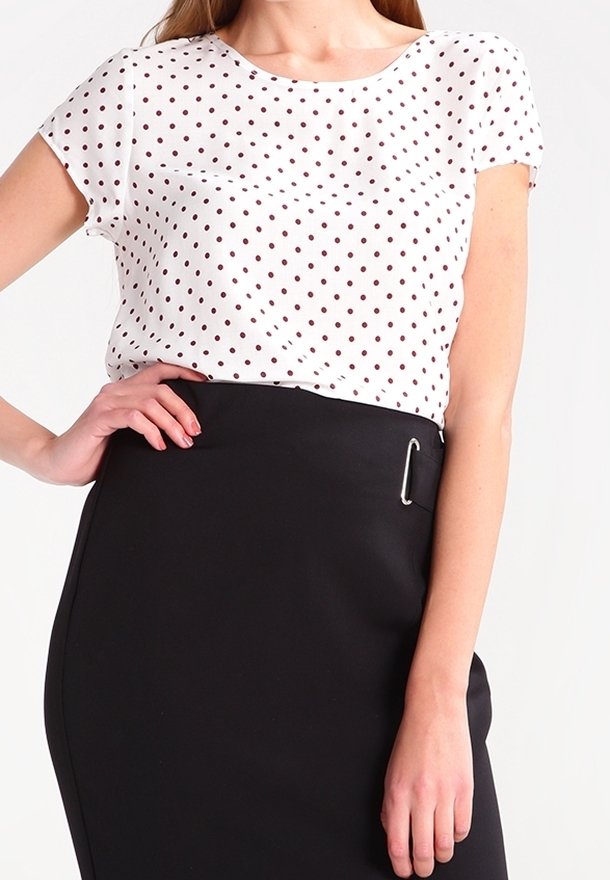 Blouse blanche à pois noirs, manches courtes, assortie à une jupe crayon noire taille haute avec une accent en épingle argentée.