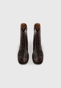 Bottines en cuir marron à lacets avec un bout arrondi et une fermeture éclair sur le côté. Elles présentent des perforations de type brogue sur le capuchon de la chaussure.