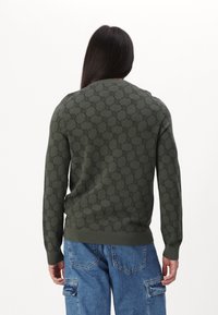 Dunkelgrüner gestrickter Pullover mit einem strukturierten Muster und gerippten Bündchen und Saum. Kombiniert mit hellblauen Cargo-Hosen.