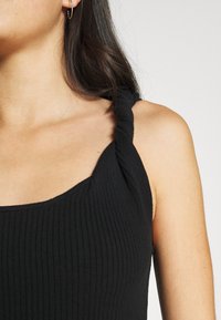 Schwarzes, geripptes Tanktop mit verdrehten Trägern und quadratischem Ausschnitt, das ein strukturiertes Strickmuster und eine figurbetonte Passform aufweist.