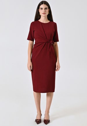 Robe bordeaux à manches courtes, mettant en avant un détail de nœud torsadé à la taille et une silhouette ajustée qui atteint le mi-mollet.